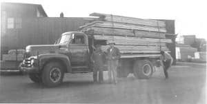 Black and white photo of two employees in front of a truck hauling lumber